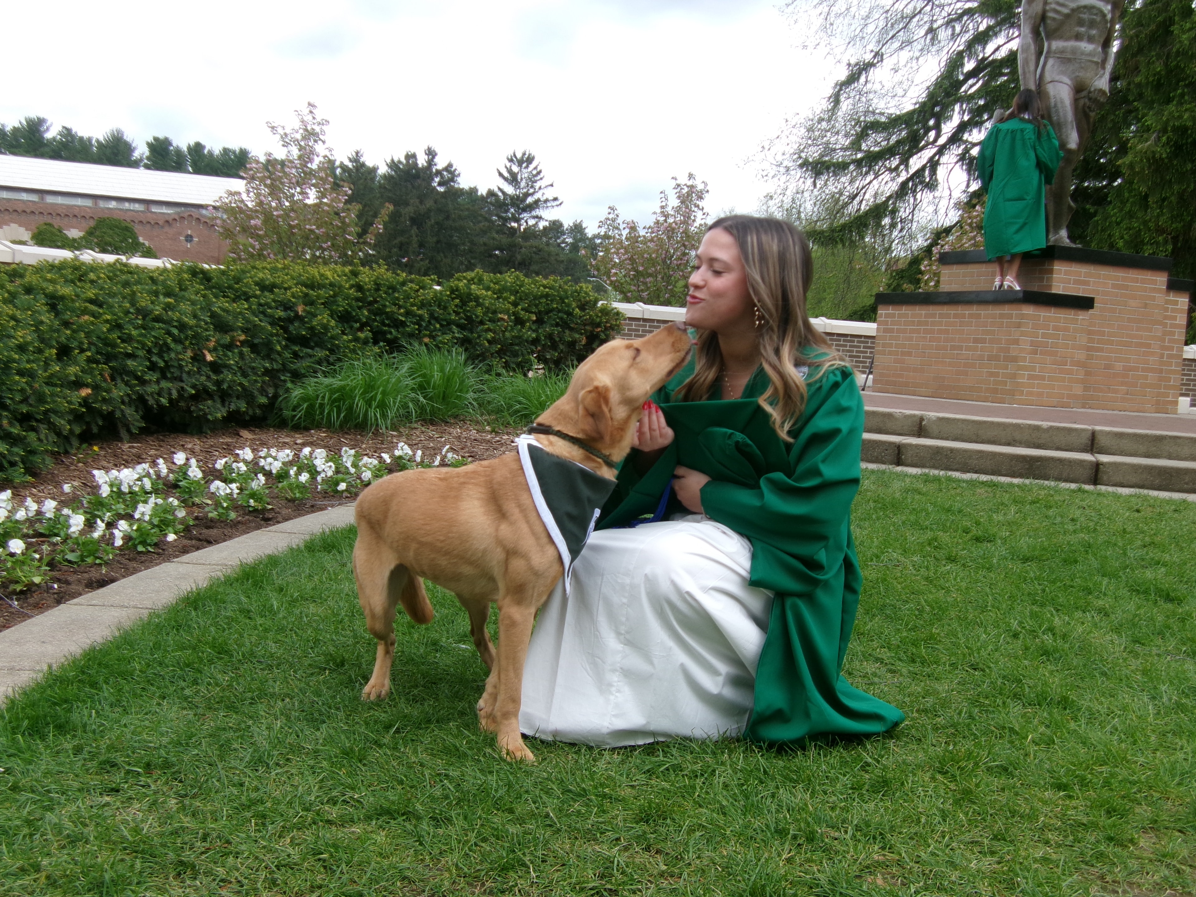 Zeke giving a kiss to an MSU graduate near the Sparty statue